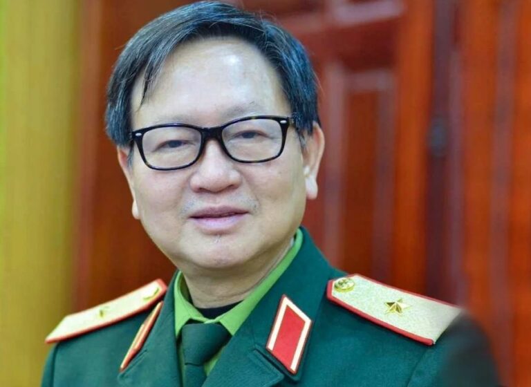 Portrait of a middle-aged man in a green military uniform with glasses, standing indoors.